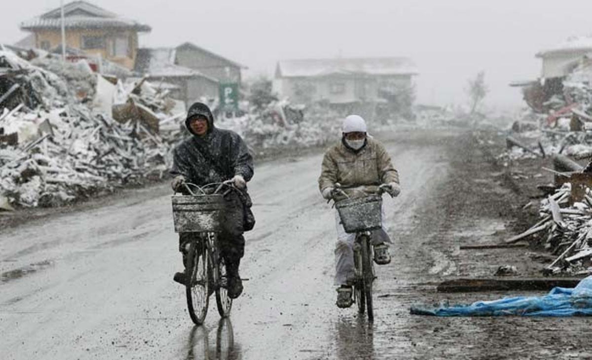 Dues persones munten en bicicleta entre les ruïnes i la neu a Natori (Japó).