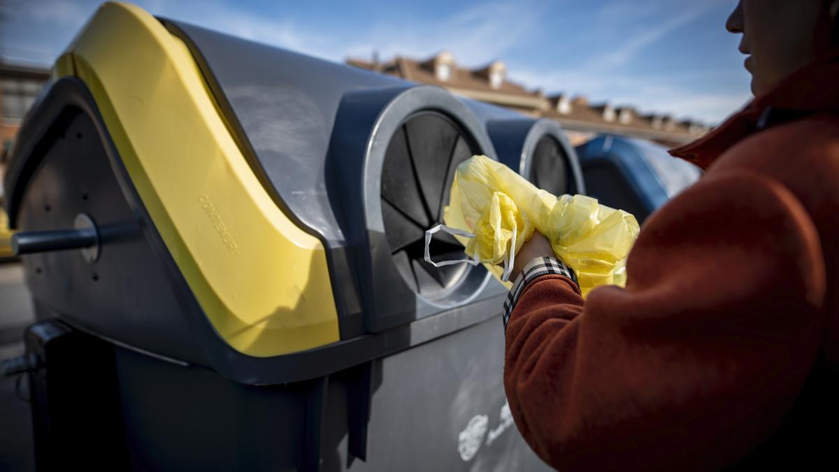 Una mujer deposita envases en un contenedor amarillo.