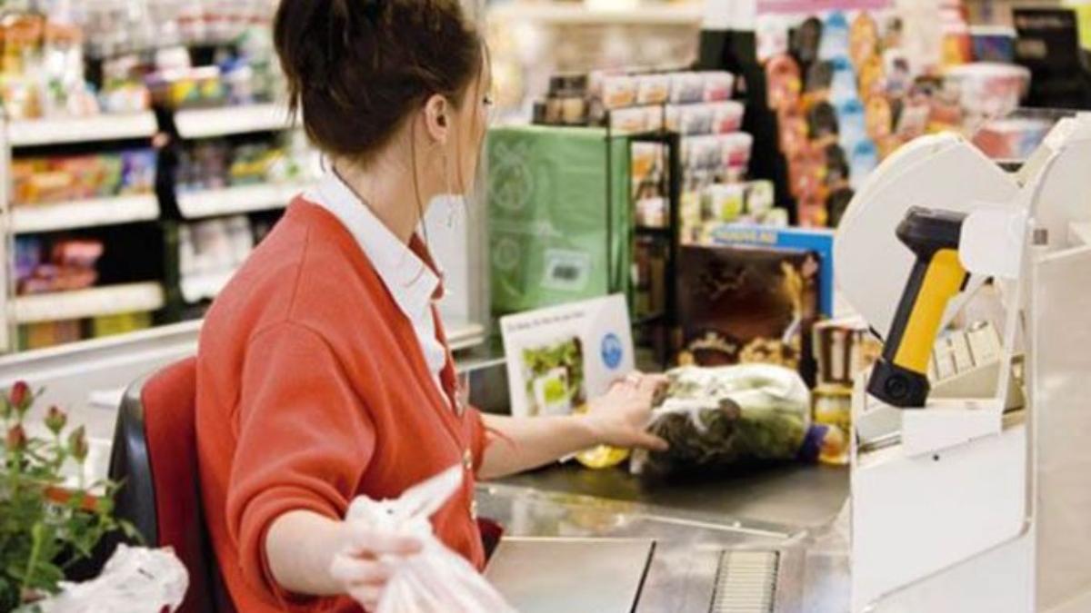 Una cajera de supermercado está cobrando a los clientes del establecimiento.