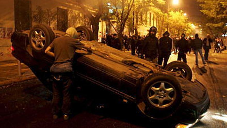 Jóvenes permanecen frente a un auto usado como barricada, durante enfrentamientos con la policía griega en el centro de Atenas (Grecia). Los disturbios iniciaron después de que un oficial de policía disparó contra un joven de 15 años de edad en un operativo policiaco.