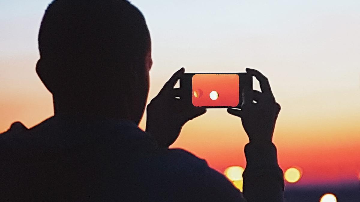 Un chico observa el Sol a través de su teléfono móvil