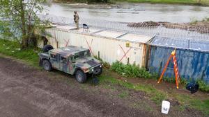 Un miembro de la Guardia Nacional de Texas inspecciona la zona sobre unos contendores colocados a modo de barrera junto al Rio Bravo.