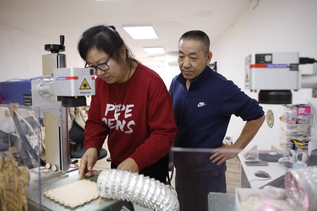 Dang Xiao Fang fertigt mit ihrem Laser personalisierte Produkte an, Lebenspartner Qing Feng Jin schaut dabei über ihre Schulter.