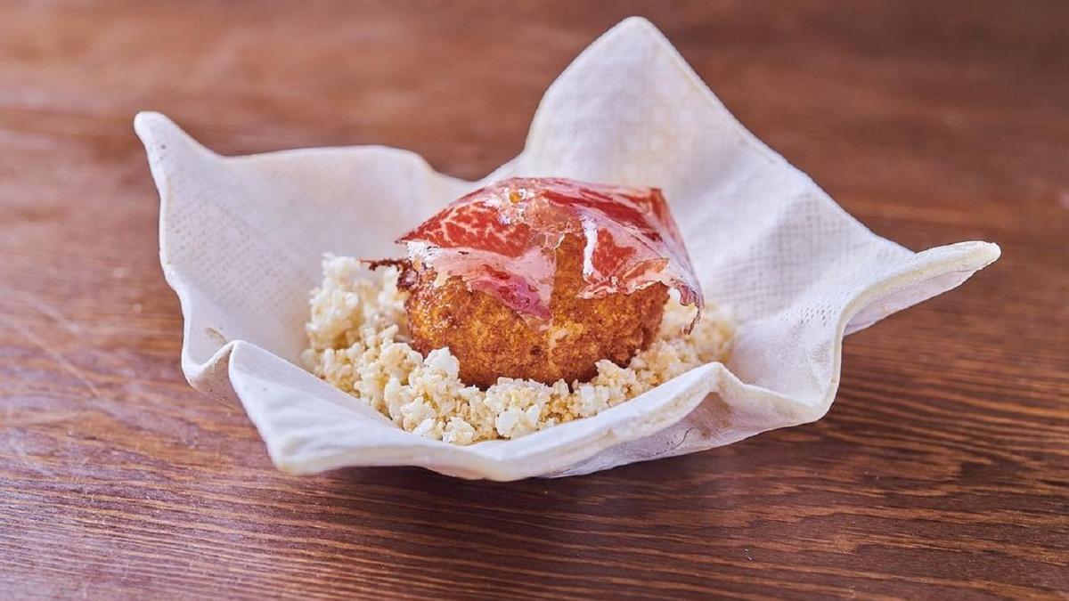 La croqueta de Cañitas Maite se sirve en una cerámica que imita las servilletas, sobre &#039;airbags&#039; de tocino de Joselito y coronada con una lámina de jamón.