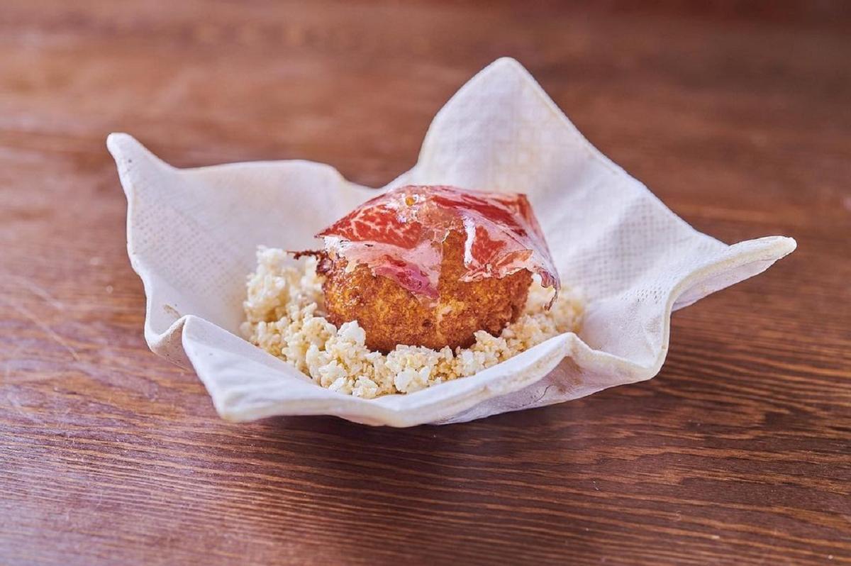 La croqueta de Cañitas Maite se sirve en una cerámica que imita las servilletas, sobre 'airbags' de tocino de Joselito y coronada con una lámina de jamón.
