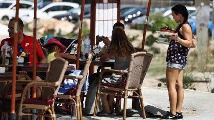 Una trabajadora de hostelería sirve mesas en una terraza este verano en Portinatx.