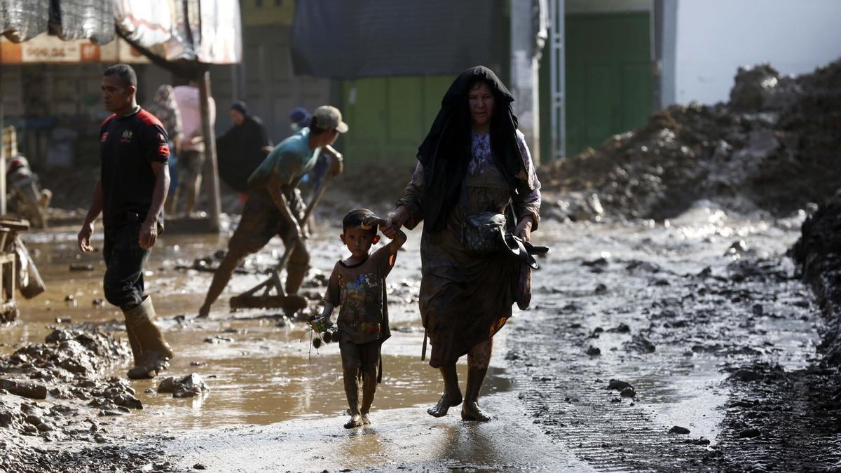 Una mujer camina junto a un niño por un barrio destrozado por las inundaciones de Indonesia.