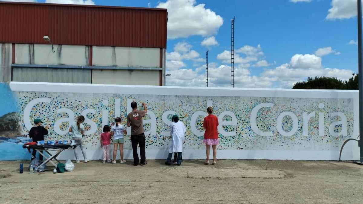 Niños y adultos escriben el nombre del pueblo en un muro.