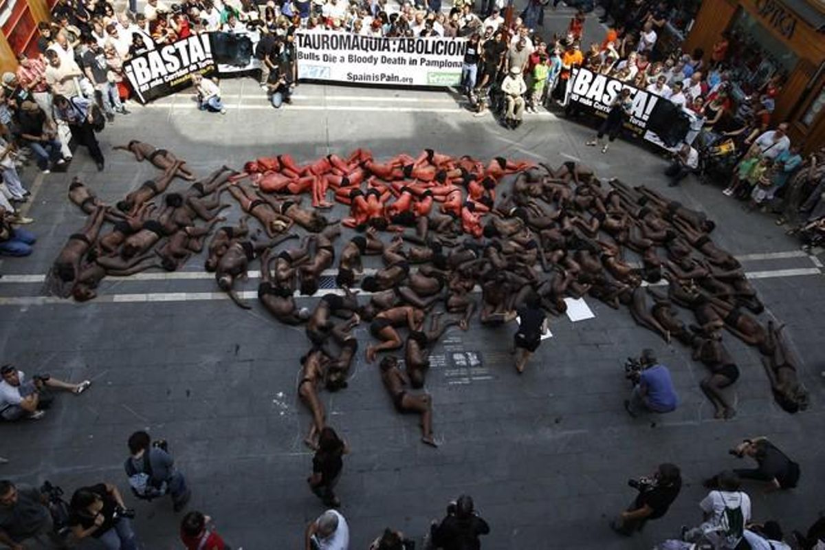 Animal {rights} {protesters} {lie} {covered} in {fake} blood and black {paint} as {they} {form} the {shape} of a bull {during} a {demonstration} in Pamplona