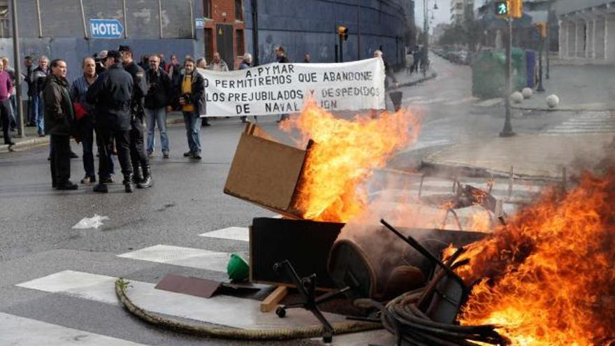 Agentes de Policía conversan con prejubilados junto a Naval Gijón, con una barricada en primer término.