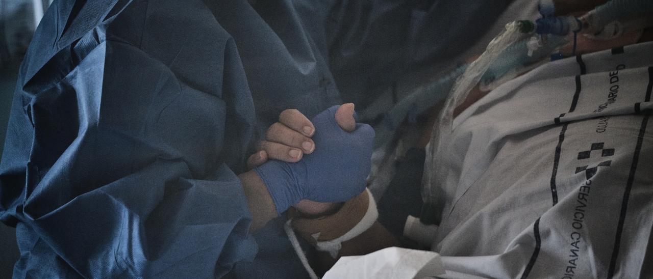 Un profesional sanitario sostiene la mano de un paciente de Covid en un hospital de Canarias.