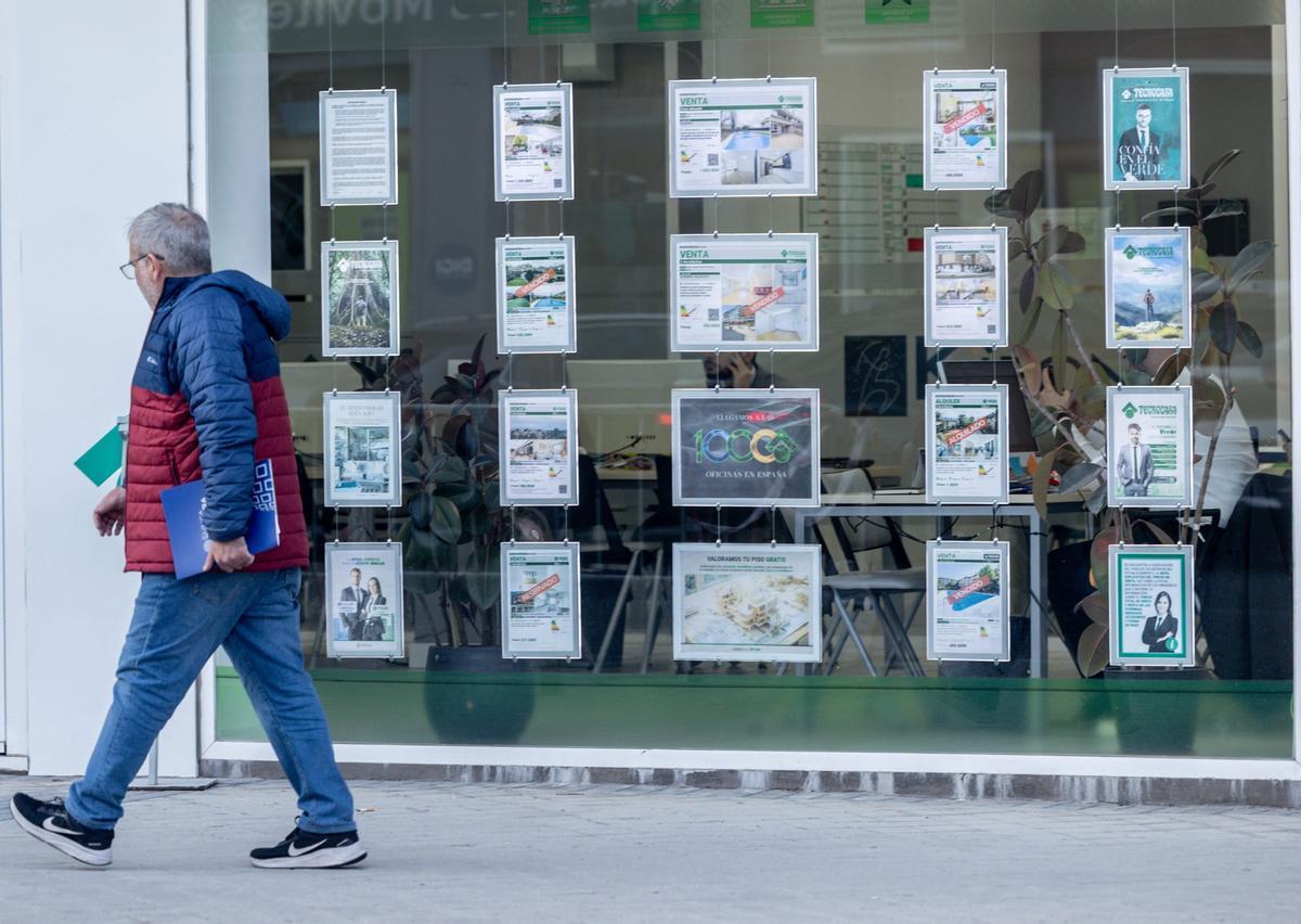 Un hombre pasa junto al escaparate de una inmobiliaria, con viviendas ofertadas, en una imagen de archivo.
