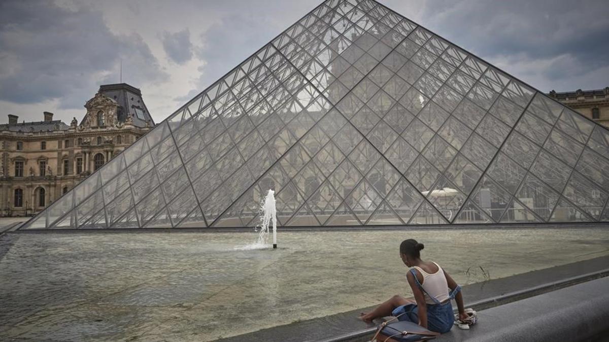 Una mujer se refresca junto a la Pirámide del Louvre, desierta de gente.