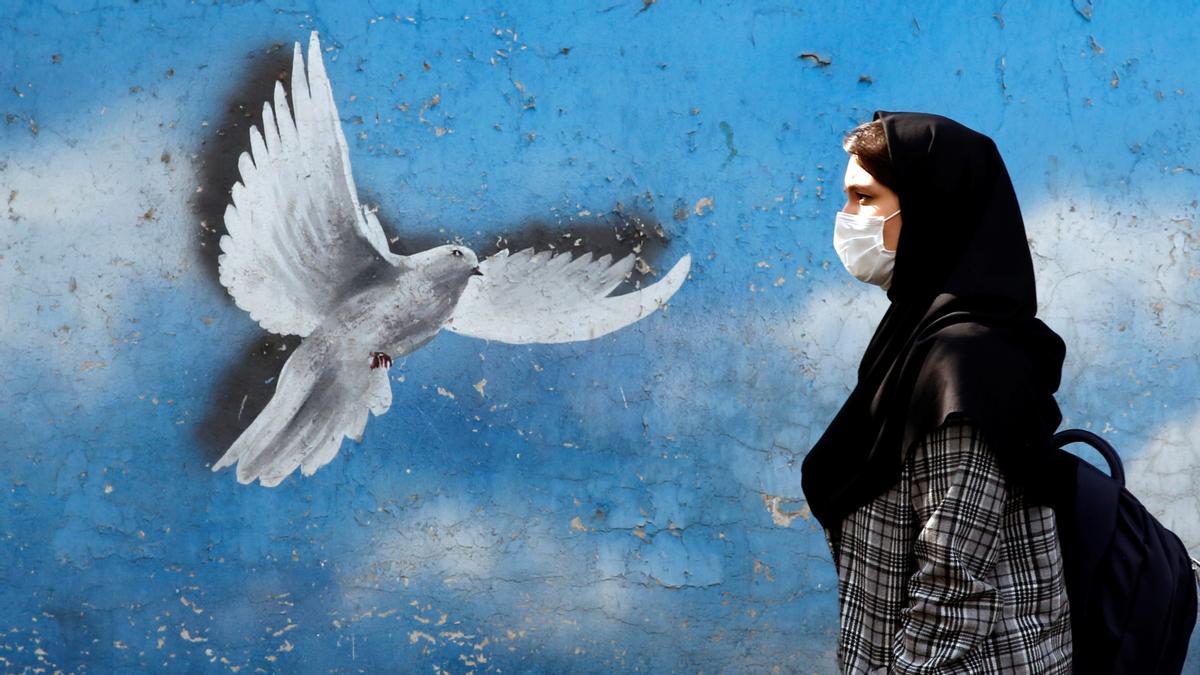 Una mujer iraní pasa frente a un mural que representa una paloma voladora en una calle de Teherán, Irán