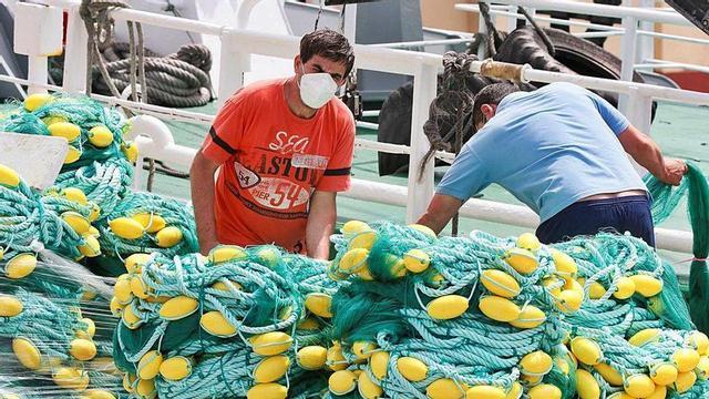 Pescadores con mascarillas preparan las redes para salir a faenar, ayer, en el puerto de Burela.