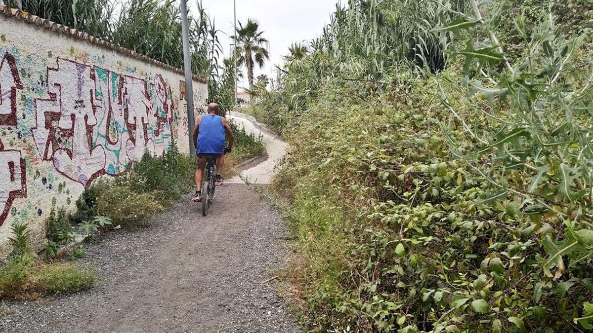 Un ciclista avanza por un camino terrizo lleno de zarzas que enlaza San Julián con los grandes centros comerciales