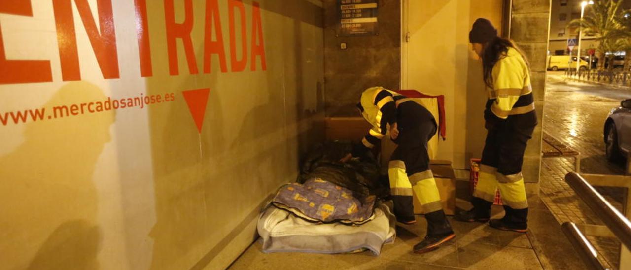 Personal interesándose por el estado de una persona que duerme en la calle, en foto de archivo.