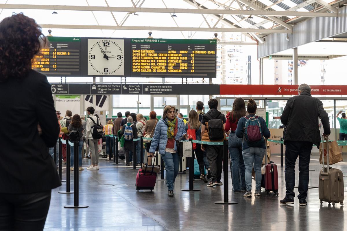 Panel de salidas y llegadas de la estación de Alicante y viajeros haciendo cola para tomar un tren.