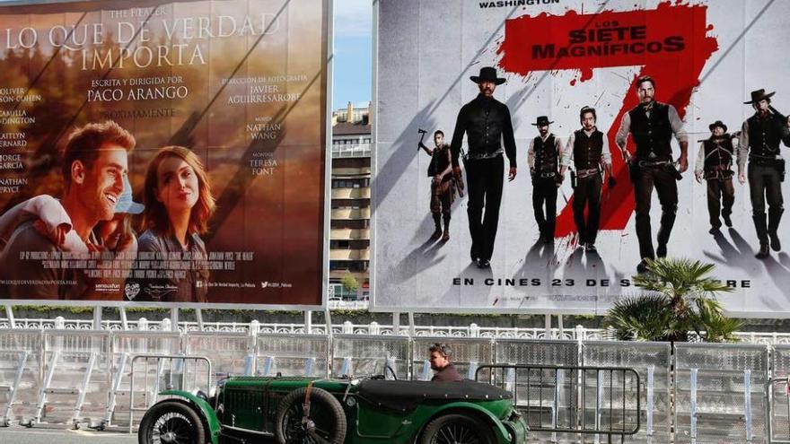 Un coche clásico pasa junto a los carteles de dos películas.