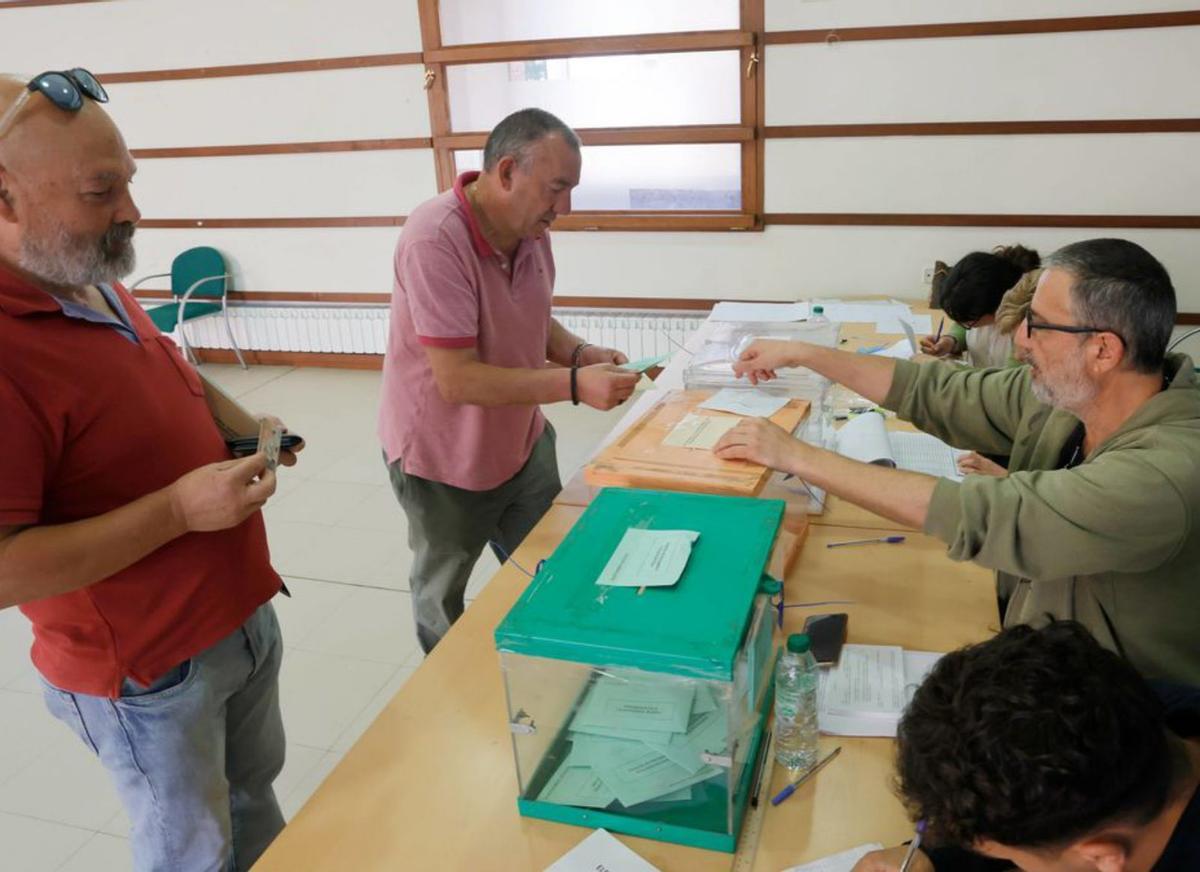 Arriba, Andrés Rojo vota mientras Julio Marina espera ante las tres urnas instaladas en Villamayor para las elecciones regionales (naranja), locales (blanca) y de las parroquias rurales (verde); sobre estas líneas, Araceli Fernández enseña su carné en la mesa electoral: por la izquierda, Carmen Fuente (apoderada del PP), Margarita Delia Cueto, vocal; Carlos Egea, presidente; y Nacho Roda, vocal. | Miki López