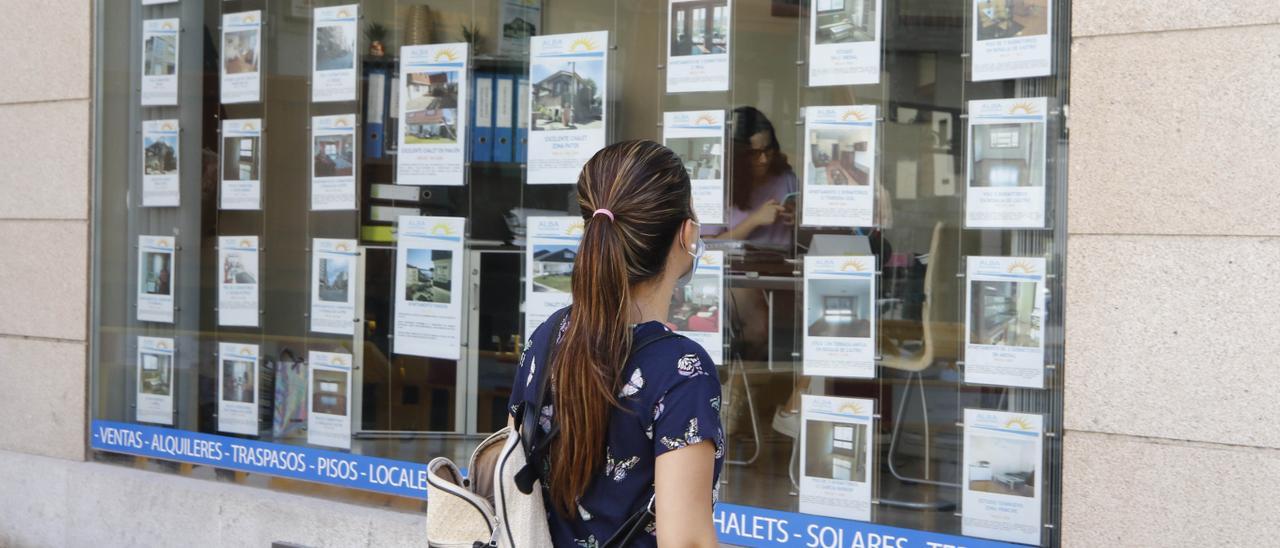 Una mujer observa las ofertas en el escaparate de una inmobiliaria.