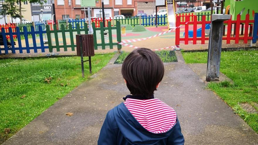 Un niño mira con deseo la zona de juegos de un parque infantil en Oviedo.