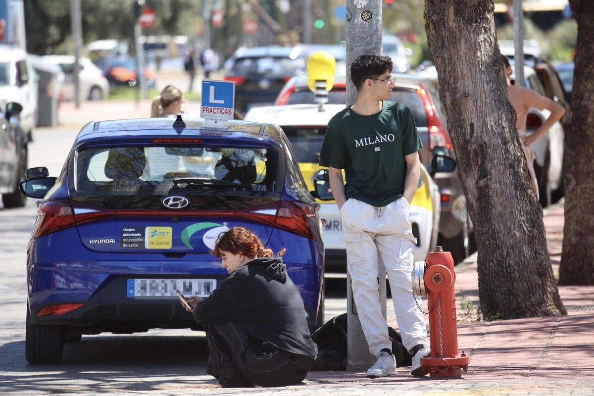 Dos jóvenes esperando a montarse en el coche de prácticas de una autoescuela, esta semana por las calles de Murcia.
