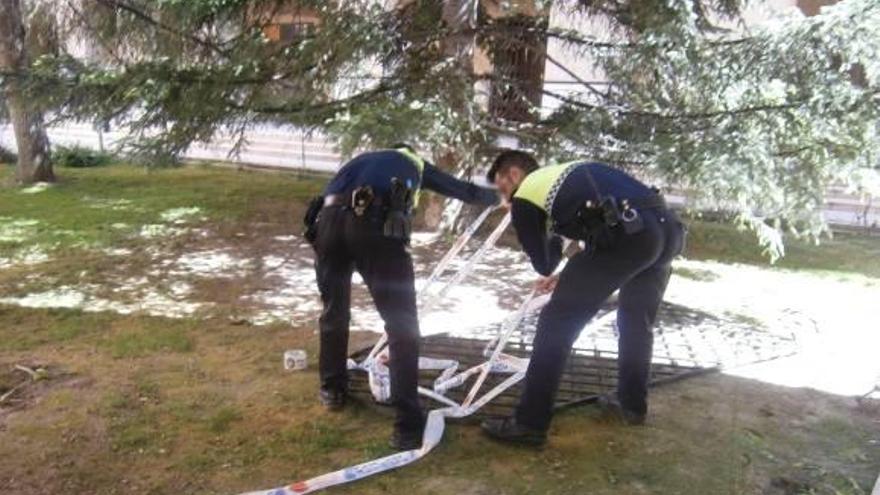 Dos policías locales precintan la puerta de hierro para proceder a su retirada para las investigaciones.