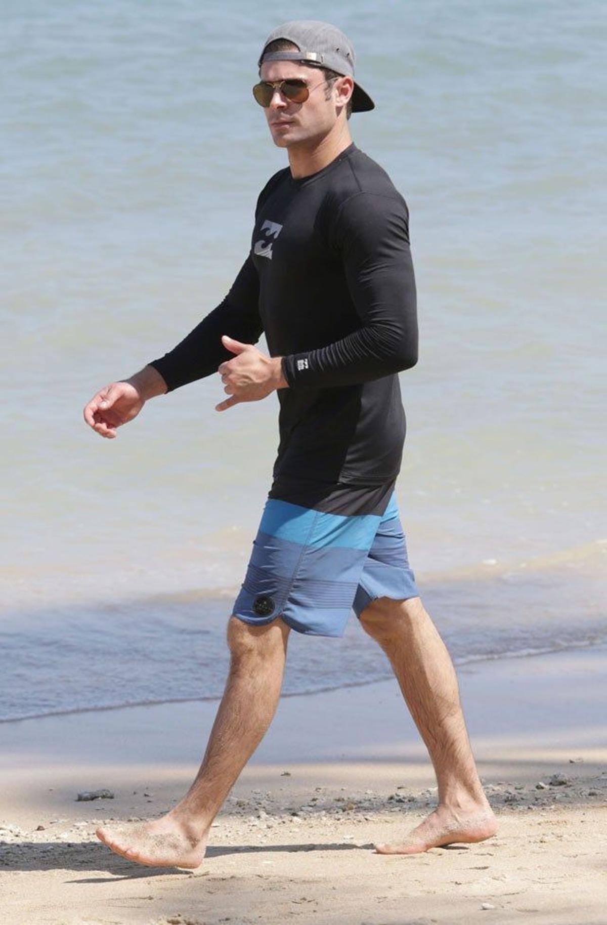 Zac Efron paseando por la playa con una gorra hacia atrás puesta