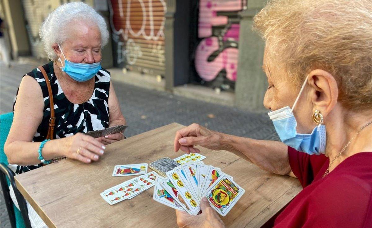 Dos mujeres con mascarilla juegan a las cartas en la calle, en el barrio del Eixample de Barcelona.