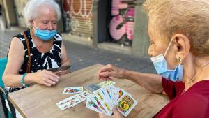 Dos mujeres con mascarilla juegan a las cartas en la calle, en el barrio del Eixample de Barcelona.