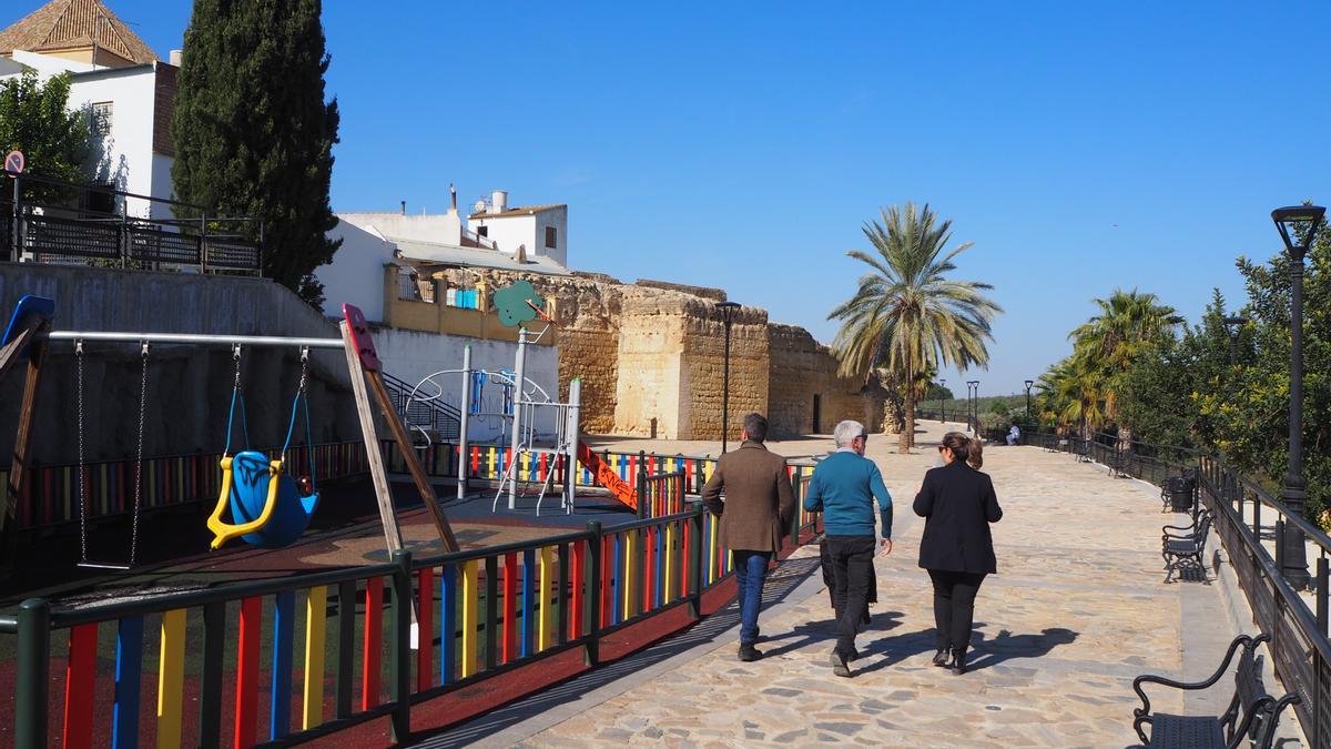 Tres vecinos caminan junto a la zona de juegos infantiles instalados en el paseo del Adarve de Santaella.