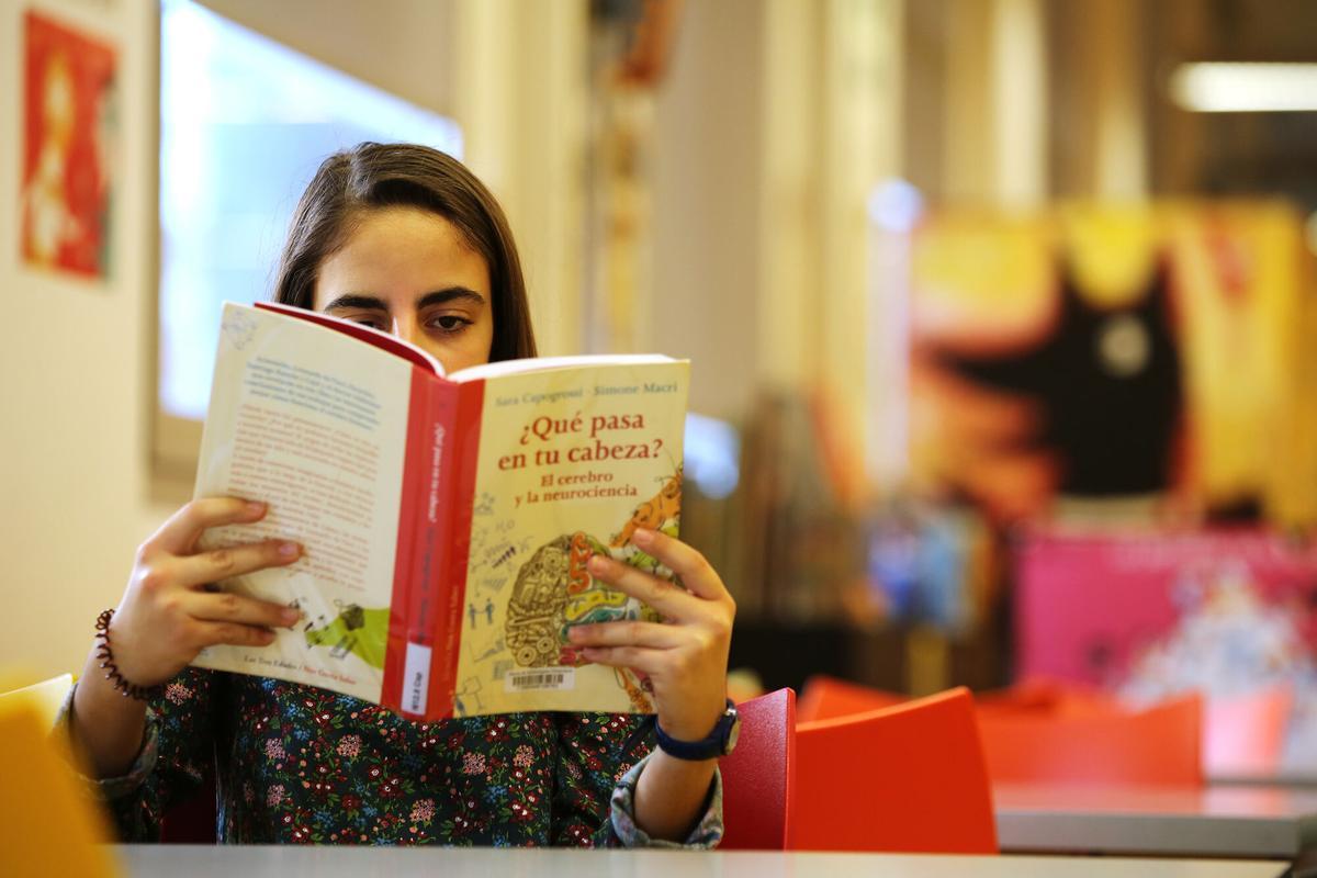 Una joven lee un libro en una biblioteca de Barcelona.