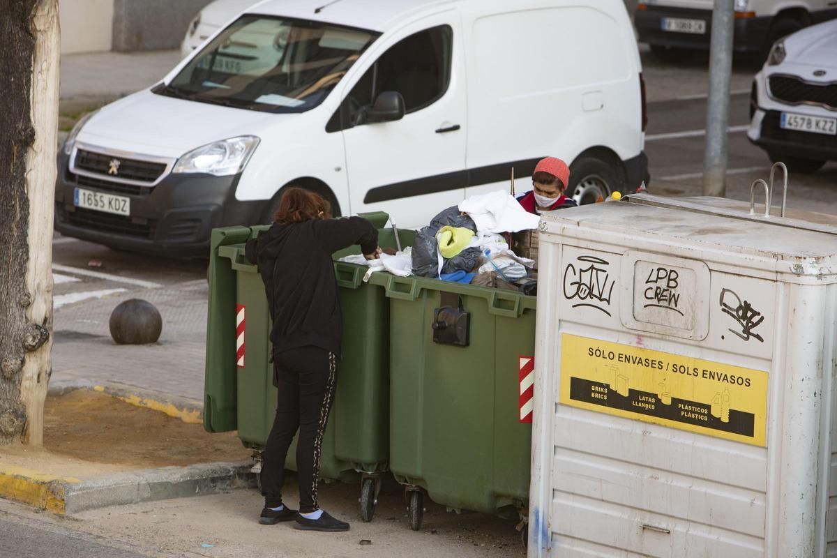 Dos personas rebuscan entre la basura, en una calle en Xàtiva.