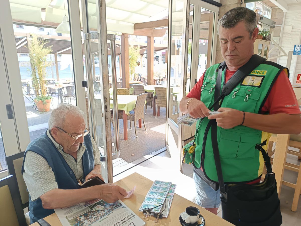 El cuponero Javier González Fernández, "Javi Cañón", atendiendo a un cliente, este martes, con el cupón de la Fiesta del Pastor, en Cangas de Onís.