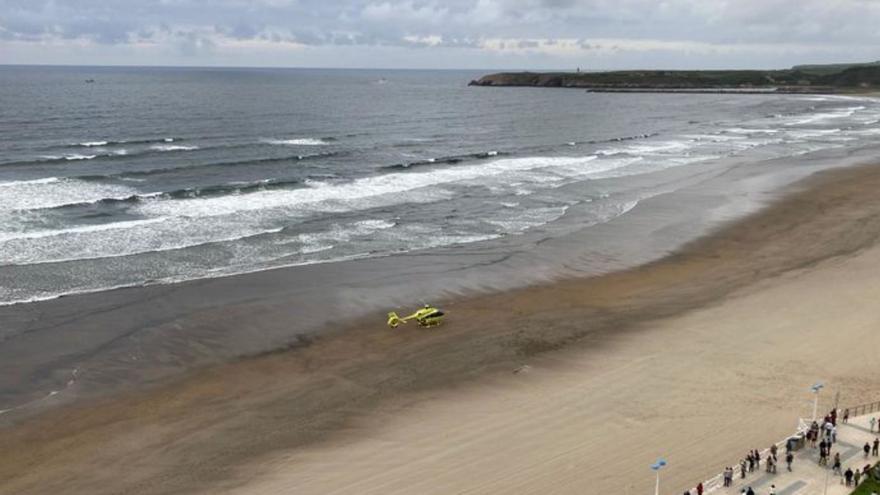 El helicóptero del 112 Asturias, en Salinas. A la derecha, la tabla qu fue hallada en el agua.
