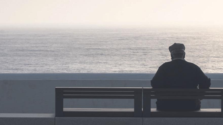 Un hombre de edad avanzada se sienta en un banco frente al mar.