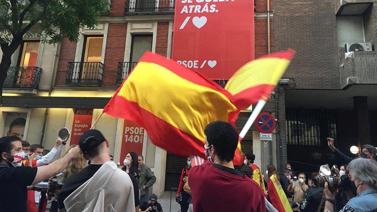 Un grupo de personas se manifiestan ante la sede del PSOE, protegida por la Policía Nacional, por la gestión de la crisis sanitaria, este domingo 17 de mayo