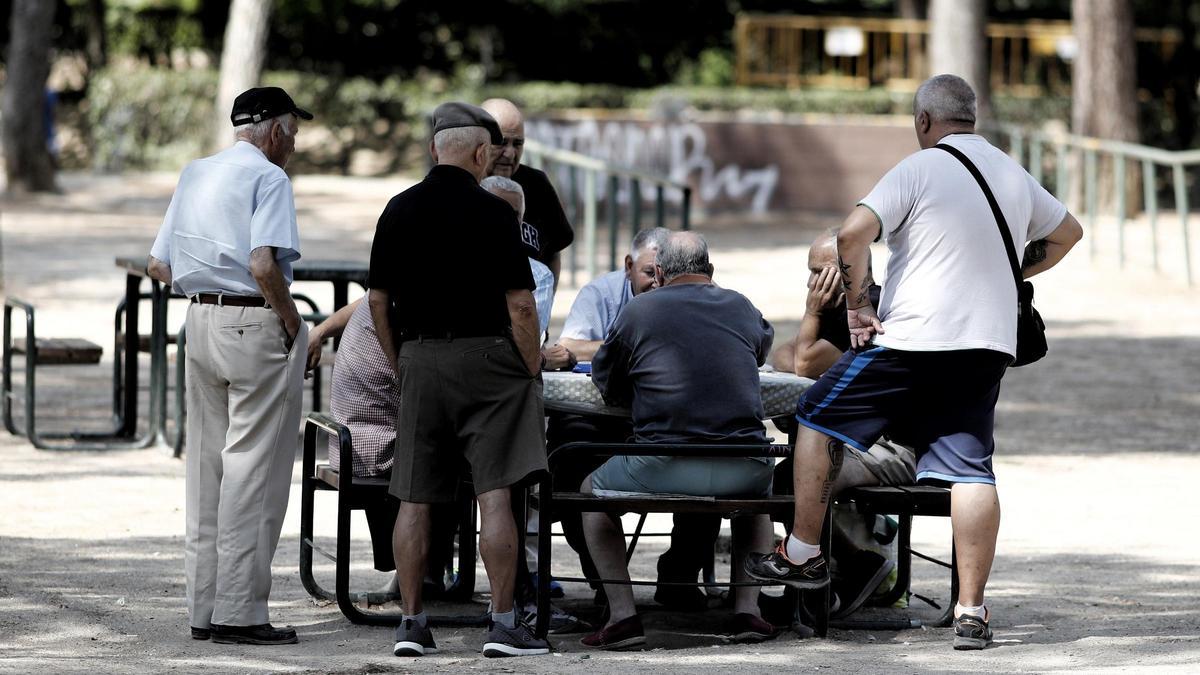 Varios pensionistas juegan a cartas en un parque.