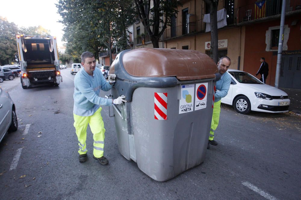 Carrers amb restes de mobiliari urbà cremat, contenidors per terra i treballadors de la brigada treballant