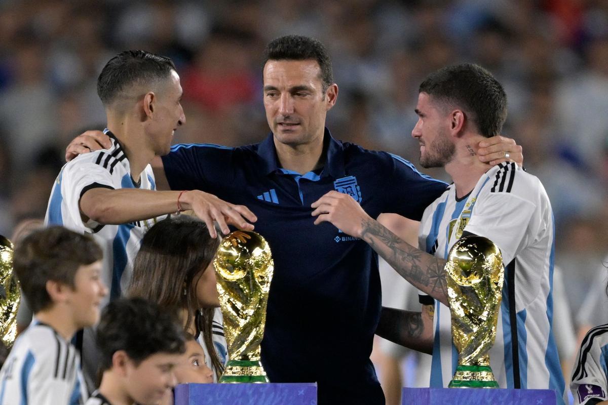 El técnico argentino Lionel Scaloni (C) abraza al mediocampista argentino Ángel Di María (L) y al mediocampista argentino Rodrigo De Paul durante una ceremonia de reconocimiento al equipo ganador de la Copa del Mundo.