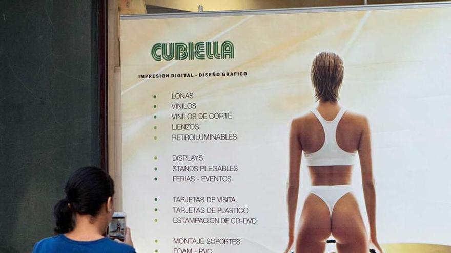 Una mujer fotografía el cartel de la tienda del barrio de El Carmen que el Principado considera sexista.