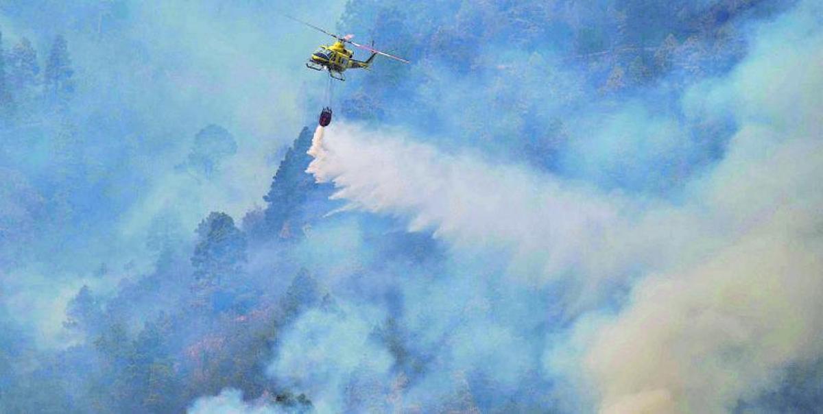 Un helicóptero realiza una descarga en medio del humo provocado por el incendio en la vertiente norte de la Corona Forestal. |  | CARSTEN W. LAURITSEN