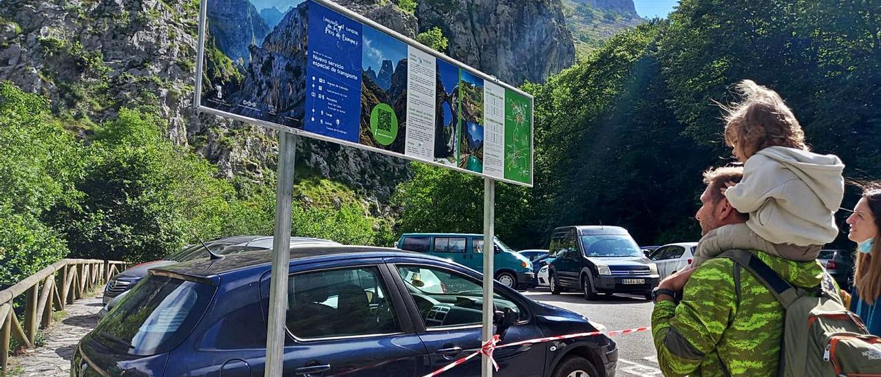 Una familia mira la nueva señalización en Poncebos, con el parking donde para el autobús, al fondo, lleno. | M. Villoria