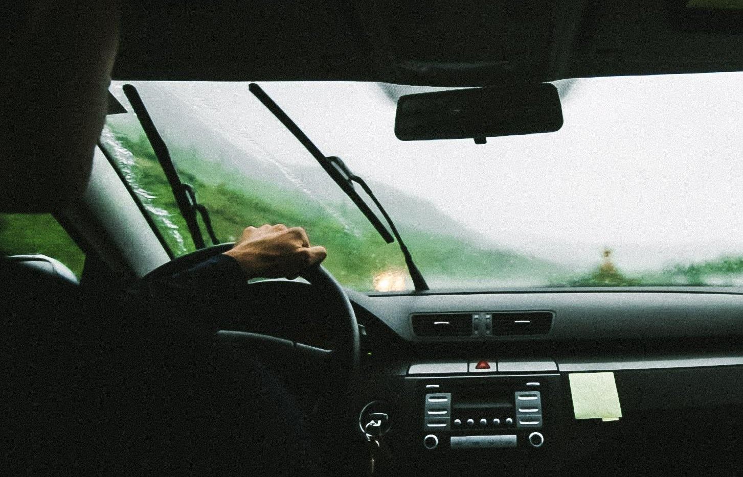 Un conductor conduce un coche con el parabrisas (los limpias) activados por lluvia