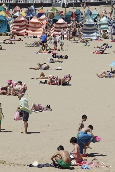 Gijoneses y visitantes se lanzan a la playa en una jornada calurosa.