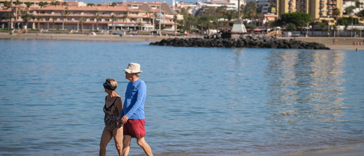 Una pareja de turistas pasea por la playa.