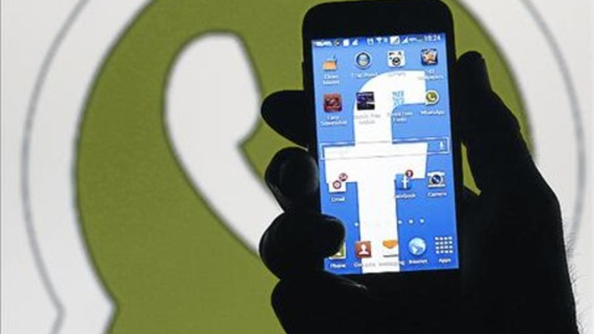 Un usuario usa un móvil frente a un logo de WhatsApp.
