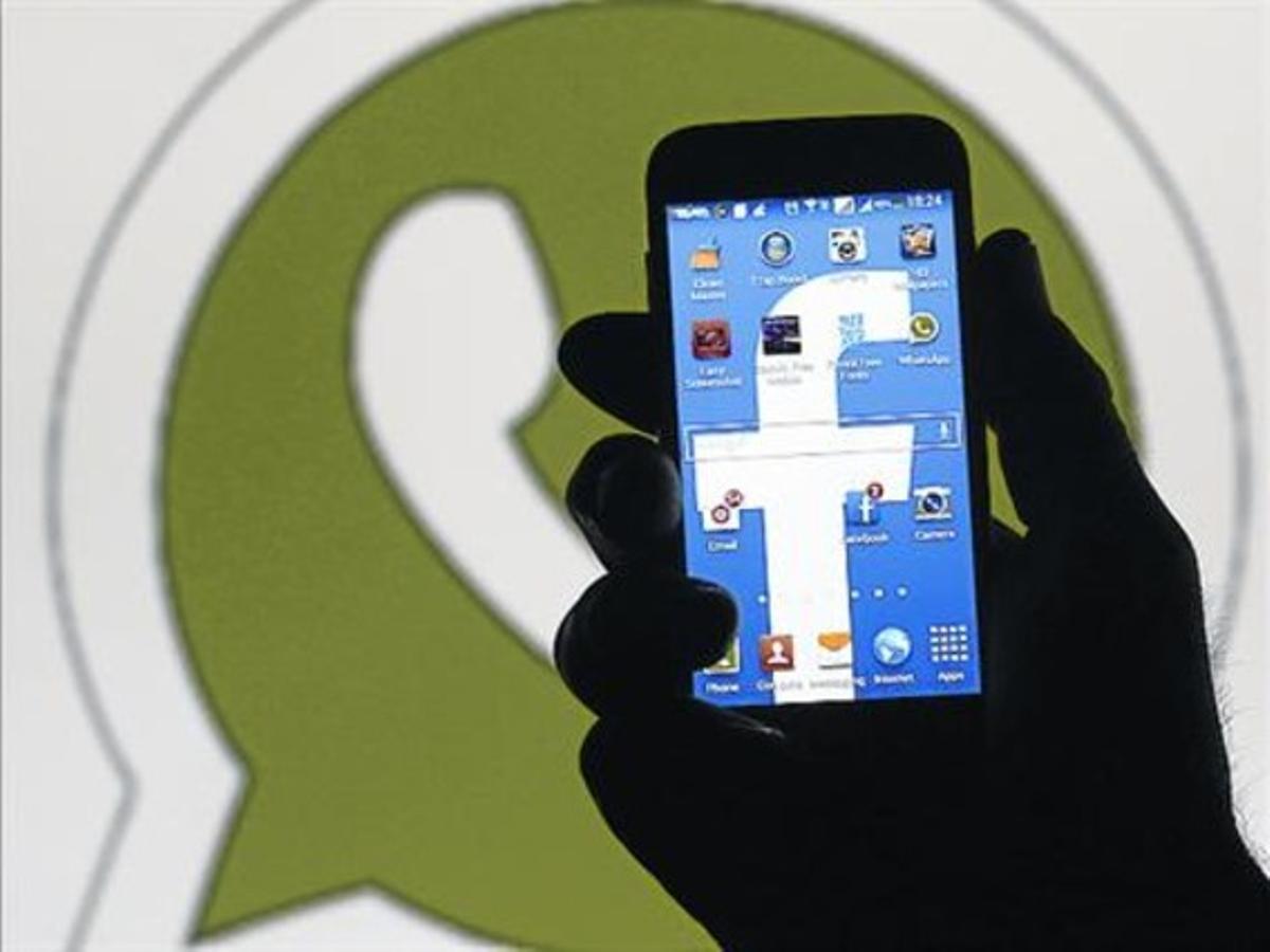 Un usuari usa un mòbil davant un logo de WhatsApp. Un usuari usa un mòbil davant un logo de WhatsApp.