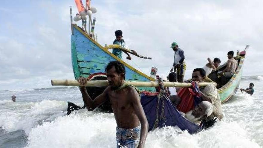 Refugiados rohinyás transportan a un hombre por la orilla del río Naf.